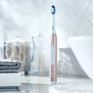 A rose gold electric toothbrush with vertical indicator lights and buttons stands upright on a bathroom counter.