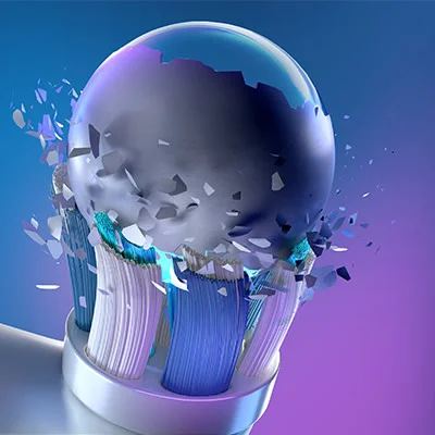 Bristles of an electric toothbrush head shattering a dark shiny sphere with fragments flying outwards.