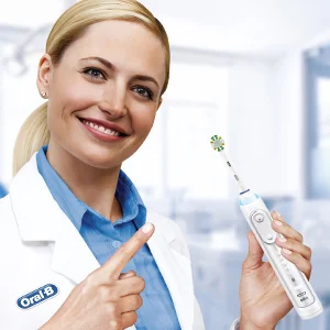 Oral-B Zahnbürste wird von einer lächelnden Frau im Arztkittel gehalten und mit dem Finger darauf gezeigt.