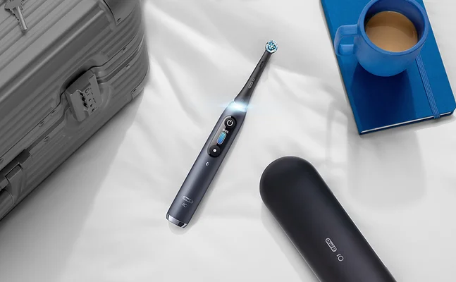 Oral-B iO elektrische Zahnbürste mit Reiseetui, neben einem Koffer, Notizbuch und einer Tasse Kaffee.