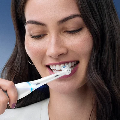 Frau putzt Zähne mit einer Oral-B iO elektrischen Zahnbürste, die saubere und gesunde Zähne verspricht.