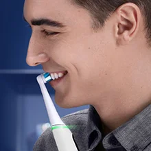 Ein Mann lächelt, während er eine Oral-B elektrische Zahnbürste benutzt, die saubere Zähne und gesundes Zahnfleisch verspricht.