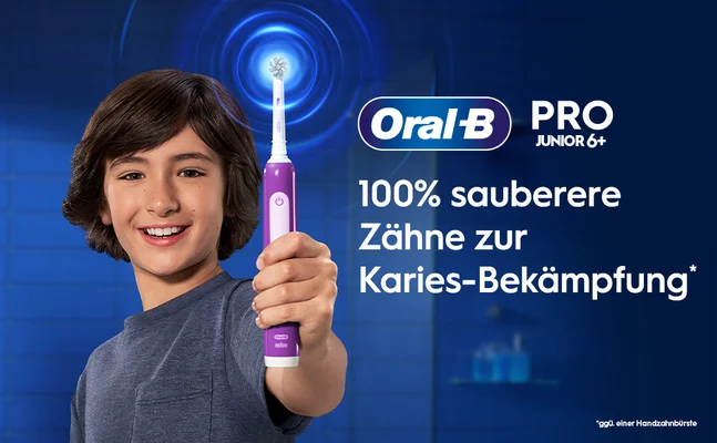 A boy smiles while holding a purple Oral-B electric toothbrush, alongside text that reads Oral-B PRO JUNIOR 6+ 100% sauberere Zähne zur Karies-Bekämpfung *ggü. einer Handzahnbürste.