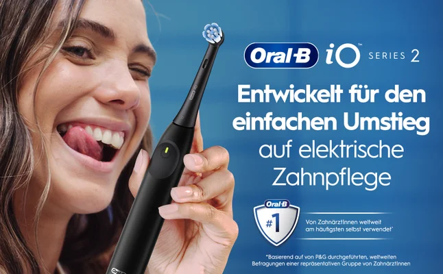 A smiling woman with long hair playfully sticking out her tongue holds an electric toothbrush against a blue background, with text that reads Oral-B iO Series 2 Entwickelt für den einfachen Umstieg auf elektrische Zahnpflege Oral-B #1 Von ZahnärztInnen weltweit am häufigsten selbst verwendet *Basierend auf von P&G durchgeführten, weltweiten Befragungen einer repräsentativen Gruppe von ZahnärztInnen.