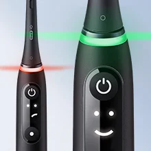 Close-up of two black electric toothbrush handles, one showing red lights and a sad face icon, the other showing green lights and a happy face icon.