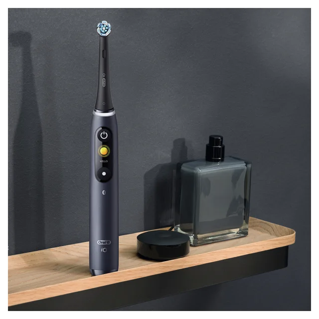Oral-B iO Zahnbürste in Anthrazit mit beleuchtetem Display und Ladestation auf Holzregal.