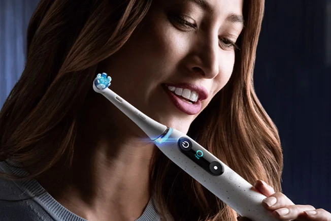 Frau lächelt beim Zähneputzen mit weißer Oral-B iO elektrischer Zahnbürste mit Leuchtring